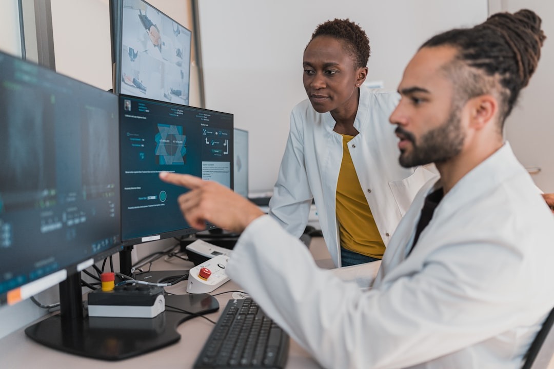 Two doctors in lab coats look at medical scans on computer screens.